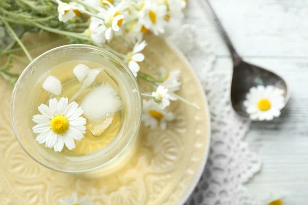 Sklo chladný Heřmánkový čaj s kostkami ledu a květy heřmánku na barevné dřevěné pozadí — Stock fotografie