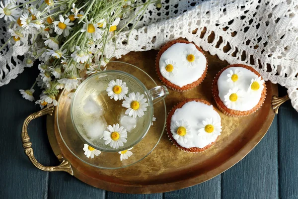 Tazza di tè alla camomilla con fiori di camomilla e gustosi muffin su vassoio, su sfondo di legno a colori — Foto Stock
