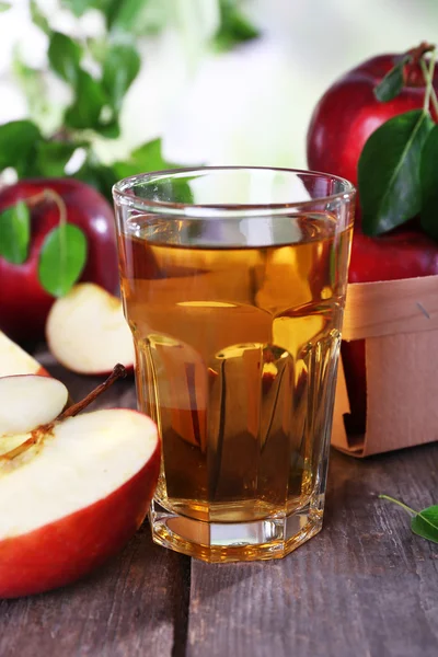 Bicchiere di succo di mela con mele rosse su tavolo di legno su sfondo sfocato — Foto Stock