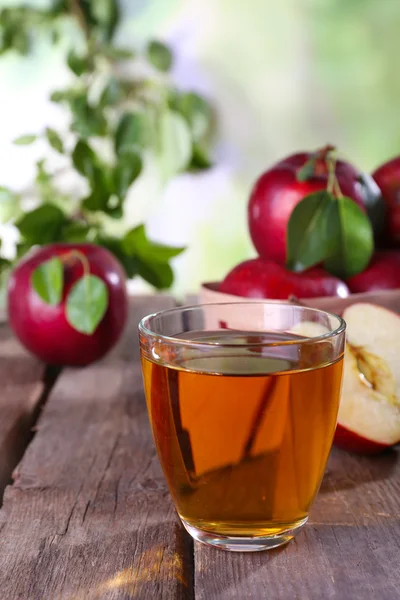 Verre de jus de pomme aux pommes rouges sur table en bois sur fond flou — Photo