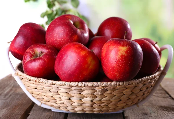 Rött äpple i rotting korg på träbord på suddig bakgrund — Stockfoto