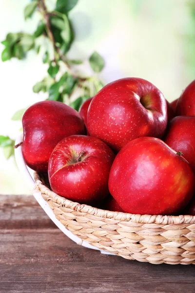 Pomme rouge dans un panier en osier sur une table en bois sur fond flou — Photo