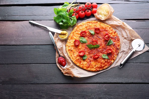 Pizza with basil and cherry tomatoes on parchment on wooden table background — Stock Photo, Image