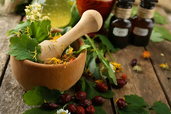 Kruiden, bessen en bloemen met mortel, op houten tafel achtergrond — Stockfoto