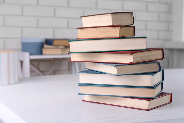 Stapel boeken op licht oppervlakte, om bakstenen muur achtergrond — Stockfoto