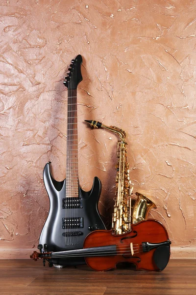Guitarra elétrica, saxofone e violino no fundo da parede marrom — Fotografia de Stock