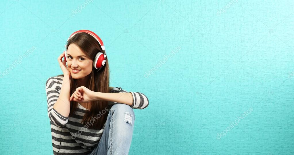 ターコイズ ブルーの壁紙の背景の上にヘッドフォンを床に座っていた若い女性 ストック写真 C Belchonock