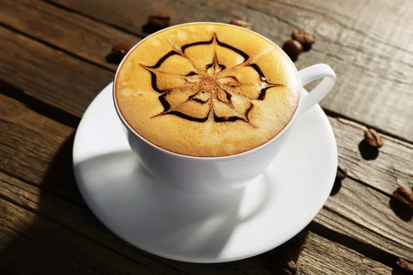 Kopje koffie latte kunst met korrels op houten achtergrond — Stockfoto