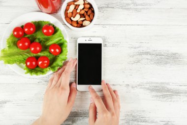Gıda ve ahşap arka plan üzerinde eller içinde hareket eden telefon