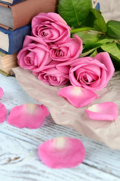 Hermosas rosas rosadas con pila de libros sobre mesa de madera con pergamino, primer plano —  Fotos de Stock