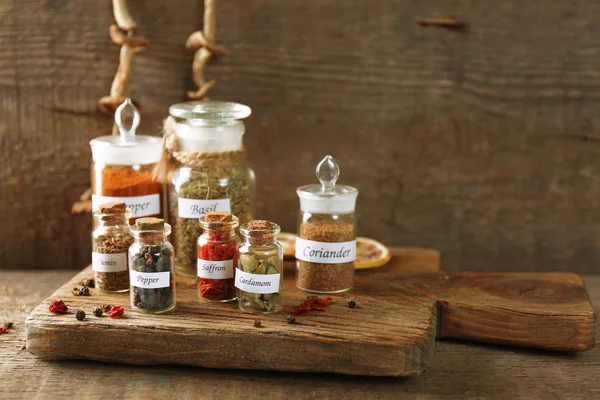 Assortment of spices in glass bottles on cutting board, on wooden background — Stock Photo, Image