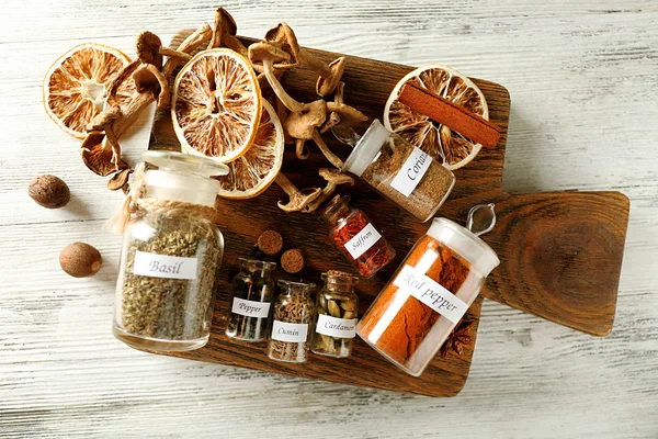 Surtido de especias en botellas de vidrio sobre tabla de cortar, sobre fondo de madera — Foto de Stock