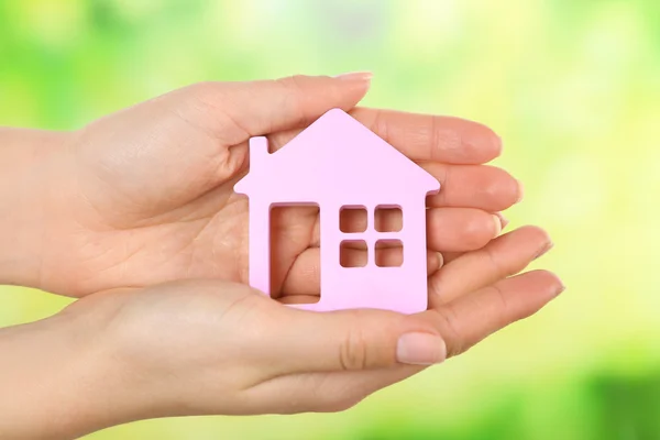 Mani femminili che tengono il modello di casa su sfondo luminoso — Foto Stock