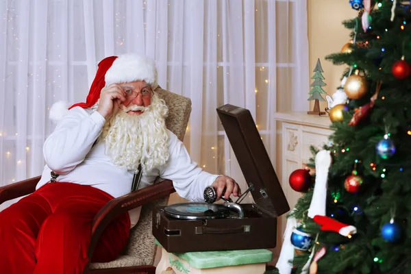 Santa Claus sitting in comfortable chair near retro turntable at home — Stock Photo, Image