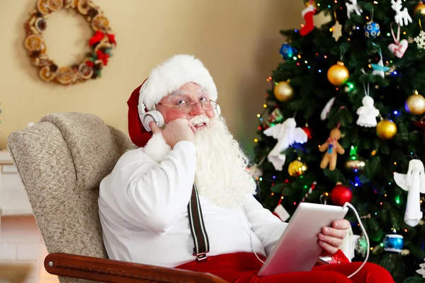 Weihnachtsmann sitzt mit digitalem Tablet im bequemen Stuhl neben dem Weihnachtsbaum zu Hause — Stockfoto
