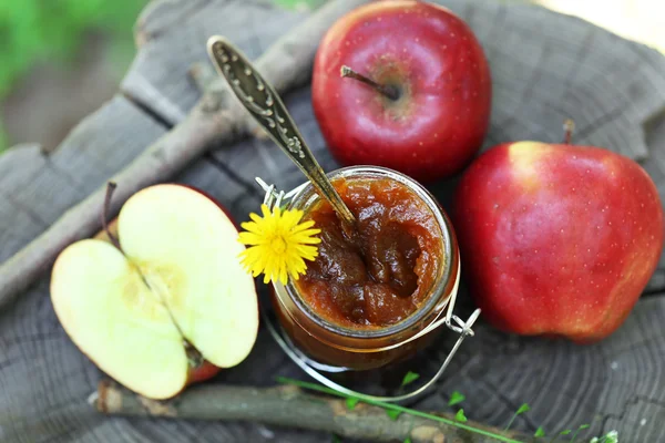 Apple jam in jar and fresh red apples on  stump outdoors