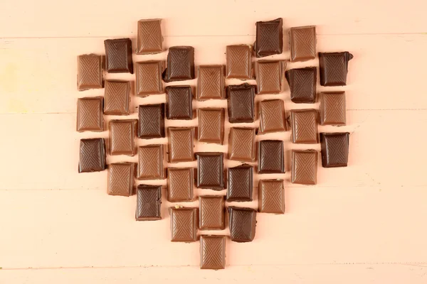 Chocolate pieces arranged in heart shape on light background — Stock Photo, Image