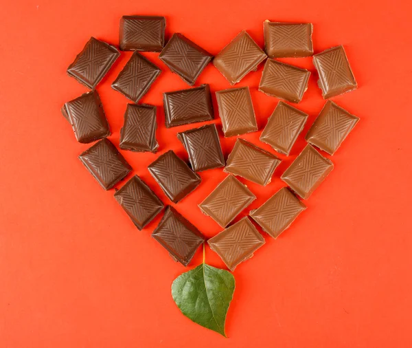Chocoladestukjes gerangschikt in hart vorm op rode achtergrond — Stockfoto