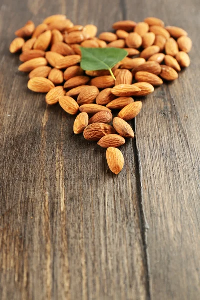 Almendras dispuestas en forma de corazón con hoja verde sobre fondo de madera —  Fotos de Stock