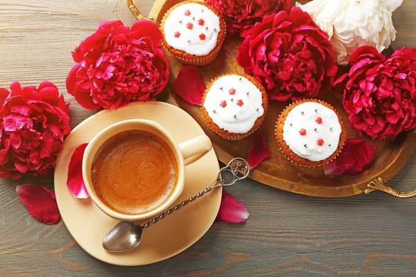 Sammansättning med kopp kaffe, muffins och pion blommor på trä bakgrund — Stockfoto