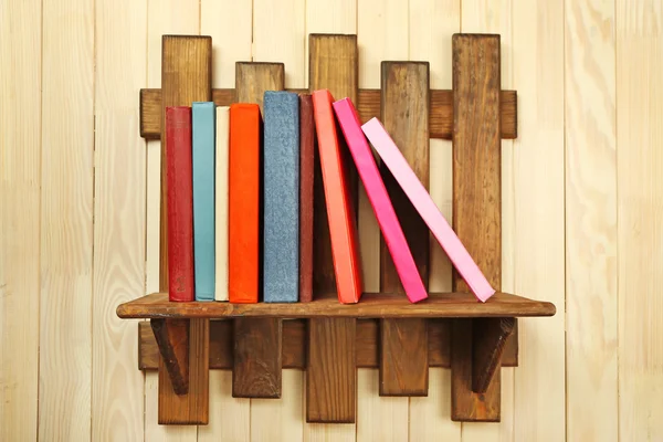 Libros coloridos en estante sobre fondo de pared de madera — Foto de Stock