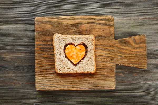 Brotscheibe mit herzförmigem Schnitt und Käse auf Holzgrund — Stockfoto
