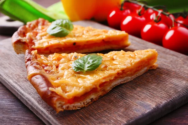 Fatias de pizza de queijo saboroso com manjericão e legumes na mesa de perto — Fotografia de Stock