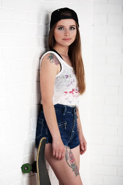 Mooie hipster meisje met skateboard op lichte achtergrond — Stockfoto