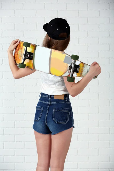 Mooie hipster meisje met skateboard op lichte achtergrond — Stockfoto