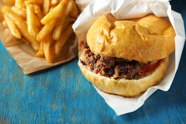 Tasty burger and french fries on wooden table — Stock Photo, Image