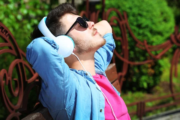 Homem com fones de ouvido descansando no banco no parque — Fotografia de Stock