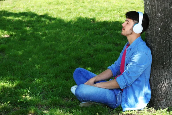 Hombre con auriculares descansando bajo el árbol en el parque — Foto de Stock