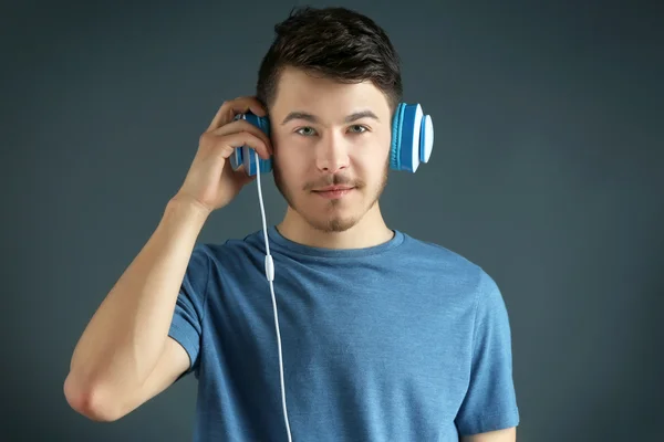 Bonito jovem ouvindo música em fundo cinza — Fotografia de Stock