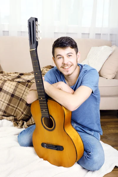 Joven con la guitarra en el suelo en la habitación — Foto de Stock