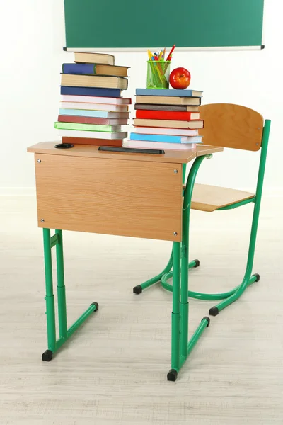 Wooden desk with books and chair in class on blackboard background — Stock Photo, Image