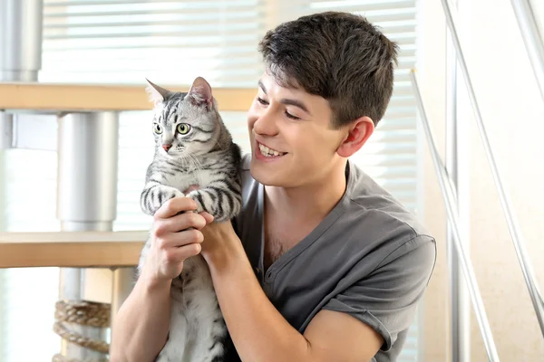 Jovem bonito com gato bonito sentado em passos em casa — Fotografia de Stock