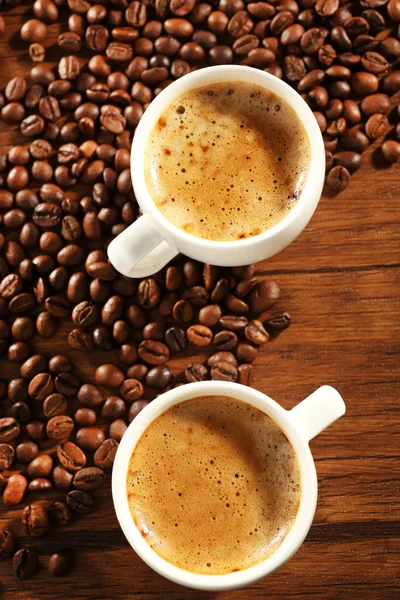 Duas xícaras de café fresco com grãos na mesa, close-up — Fotografia de Stock