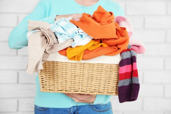 Woman holding basket with heap of different clothes, on bricks wall background — Stock Photo, Image