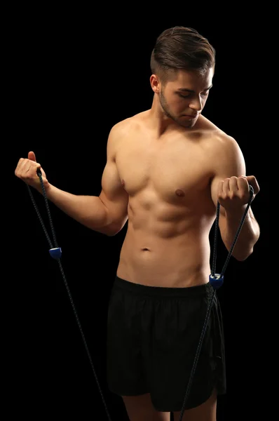 Muscle young man exercising with resistance band on dark background — Stock Photo, Image