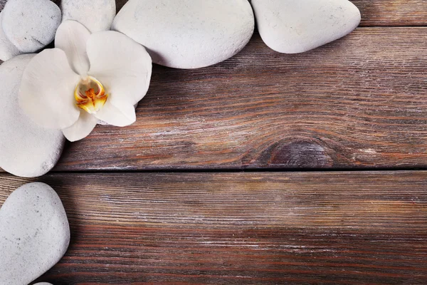 Pedras de spa e flor de orquídea em fundo de madeira — Fotografia de Stock