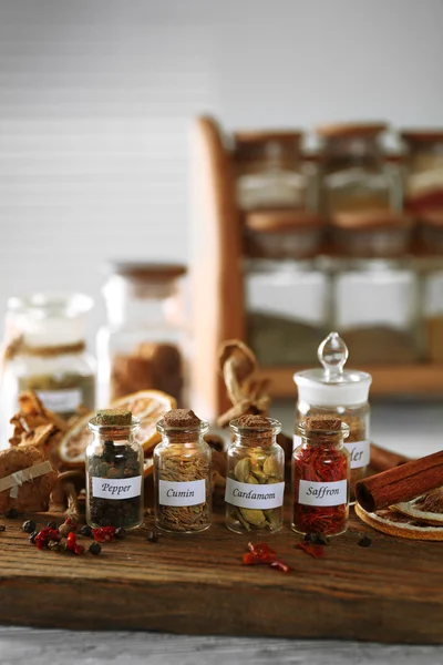 Assortment of spices in glass bottles on cutting board, on wooden background — Stock Photo, Image