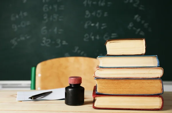 Högen med böcker på skrivbord, på blackboard bakgrund — Stockfoto