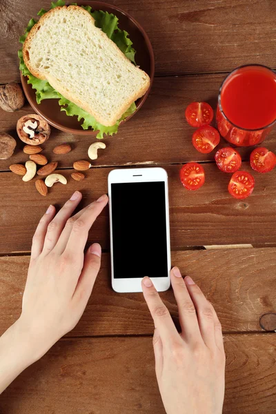 Alimentación y teléfono móvil en manos femeninas sobre fondo de madera —  Fotos de Stock