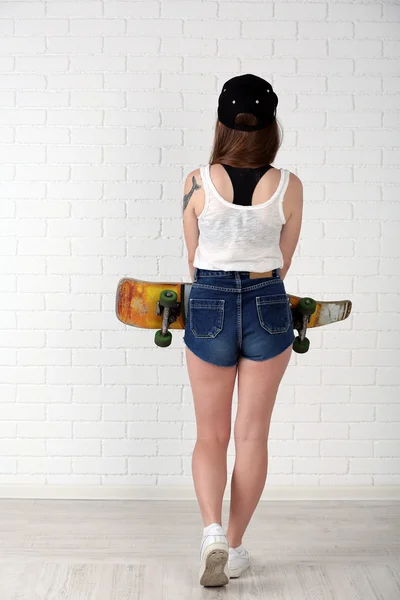 Vacker hipster flicka med skateboard på ljus bakgrund — Stockfoto