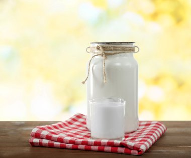 Retro can for milk and glass of milk on wooden table, on bright background