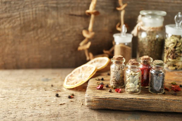 Sortimento de especiarias em garrafas de vidro na placa de corte, no fundo de madeira — Fotografia de Stock