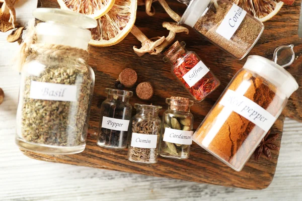 Assortment of spices in glass bottles on cutting board, on wooden background — Stock Photo, Image