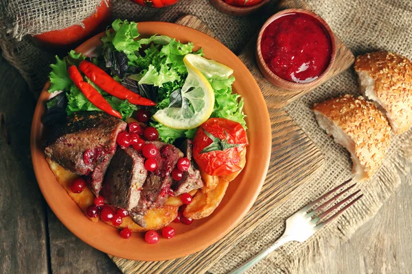 Carne arrosto saporita con salsa di mirtilli rossi, insalata e verdure arrosto sul piatto, su sfondo di legno — Foto Stock