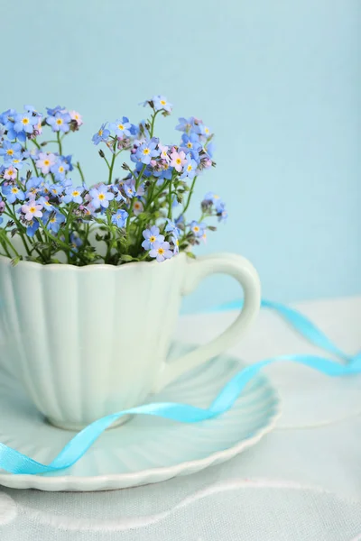 Forget-me-nots blommor i cup, på blå bakgrund — Stockfoto