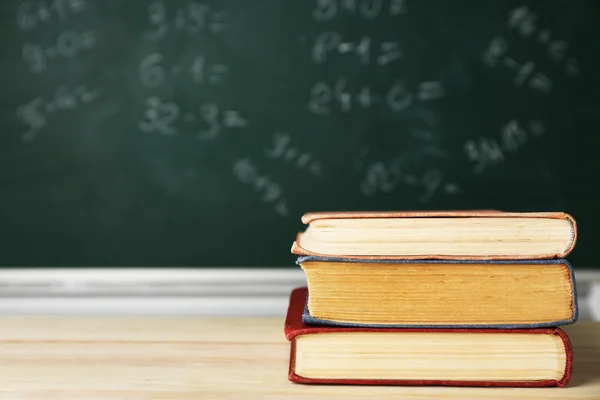 Stack of books on desk, on blackboard background — Stock Photo, Image